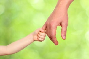 a father holds the hand of a small child on a green background