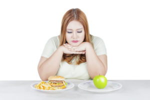 67352677 - portrait of overweight woman looks doubtful to choose a fresh apple fruit or hamburger, isolated on white background