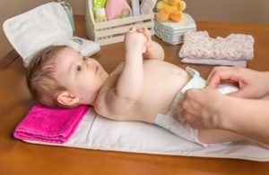 26786679 - mother changing diaper of adorable baby with a hygiene set for babies on the background