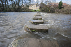 45012451 - stepping stones across a small river in english rural village countryside scene.