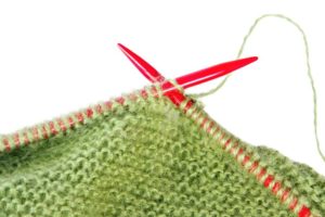 2455150 - knitting with green fluffy wool, on red knitting needles. close-up view, over white.